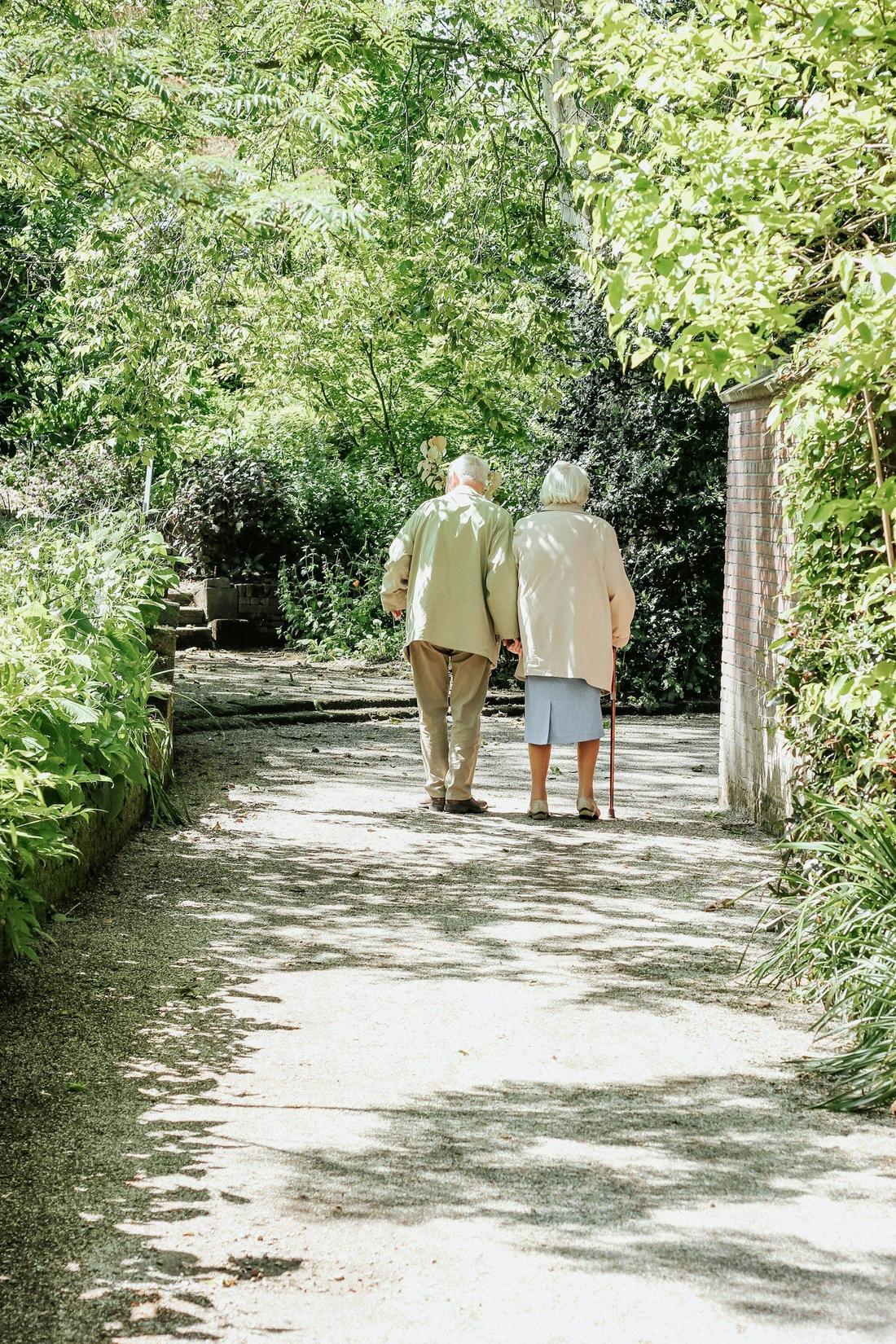Pareja de adultos mayores caminando por un sendero arbolado